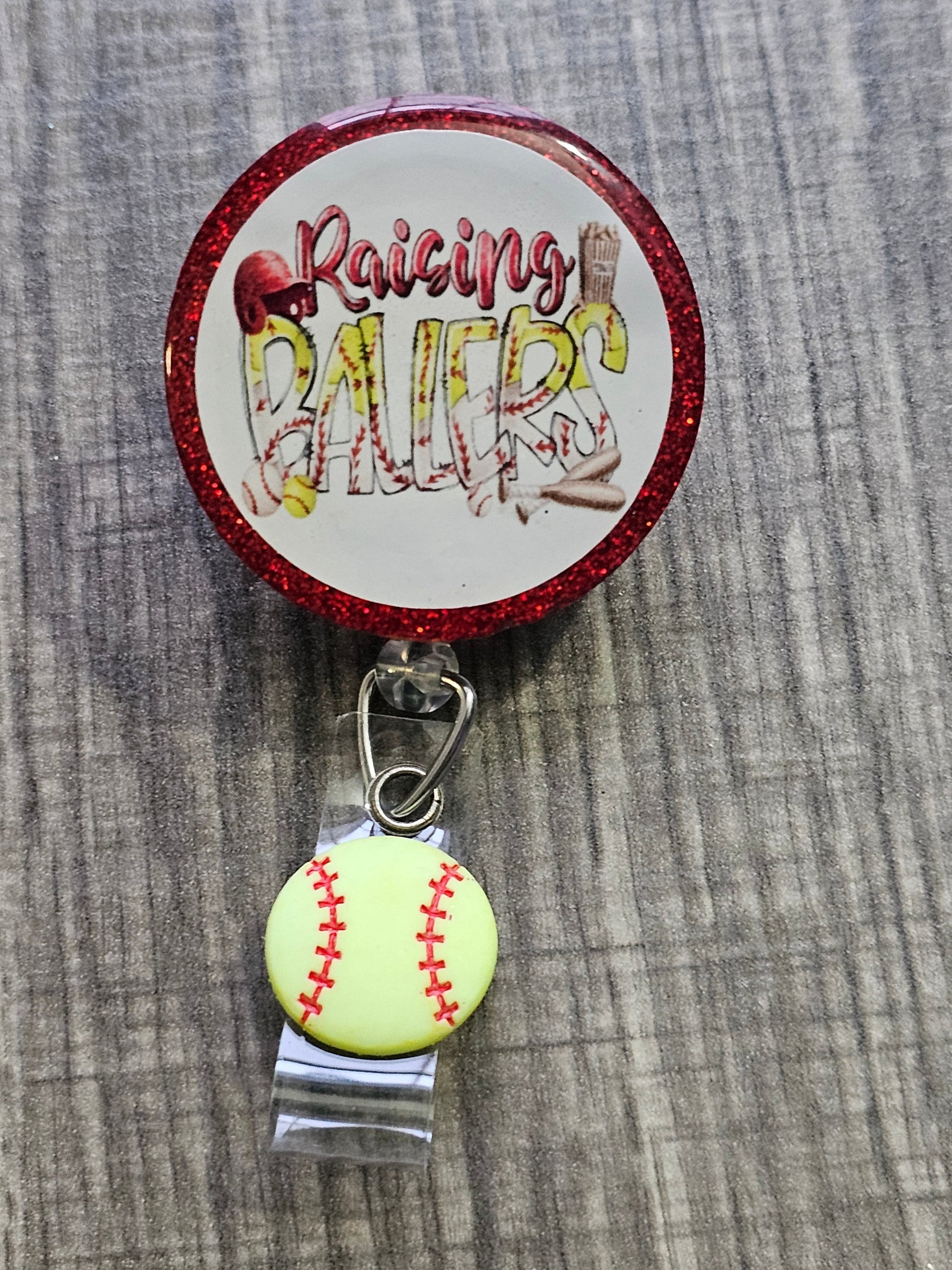  A Badge Reel with the statement Raising Ballers with a softball clip .