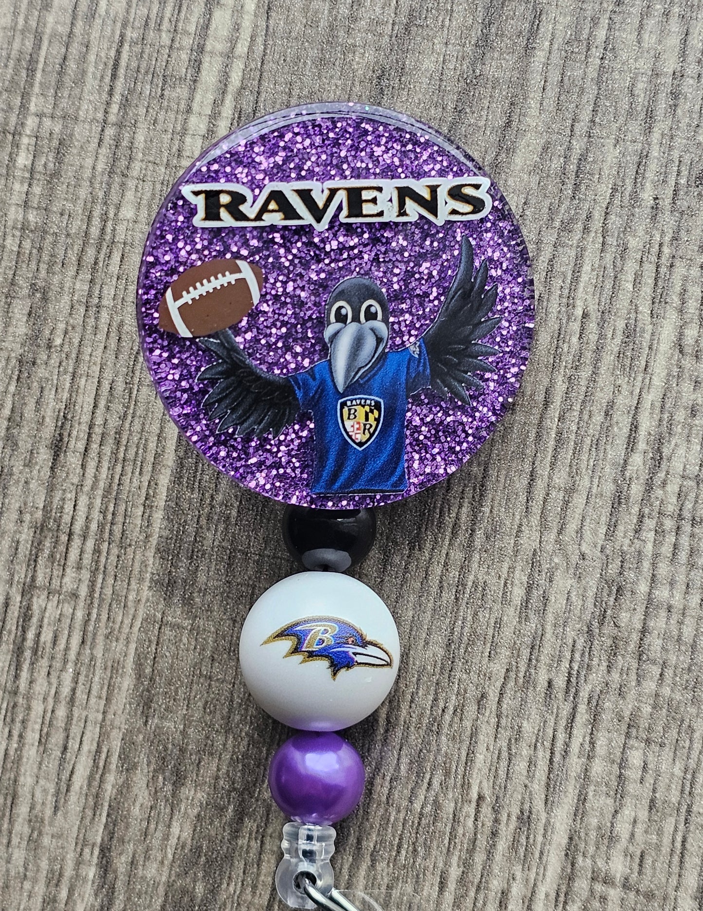 A purple badge reel featuring the Baltimore Ravens mascot holding a football along with the word Ravens above it 