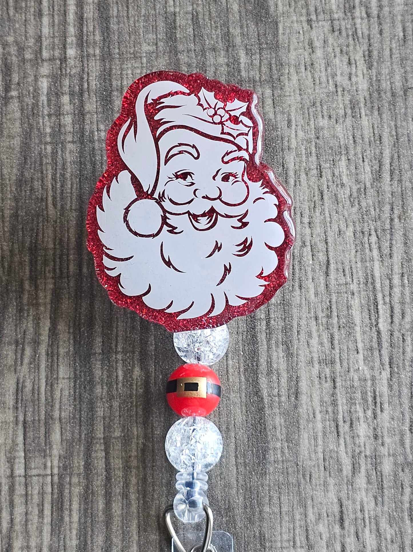 A badge reel that is shaped like santa's head while featuring it with a bright smile, and a decorated hat.