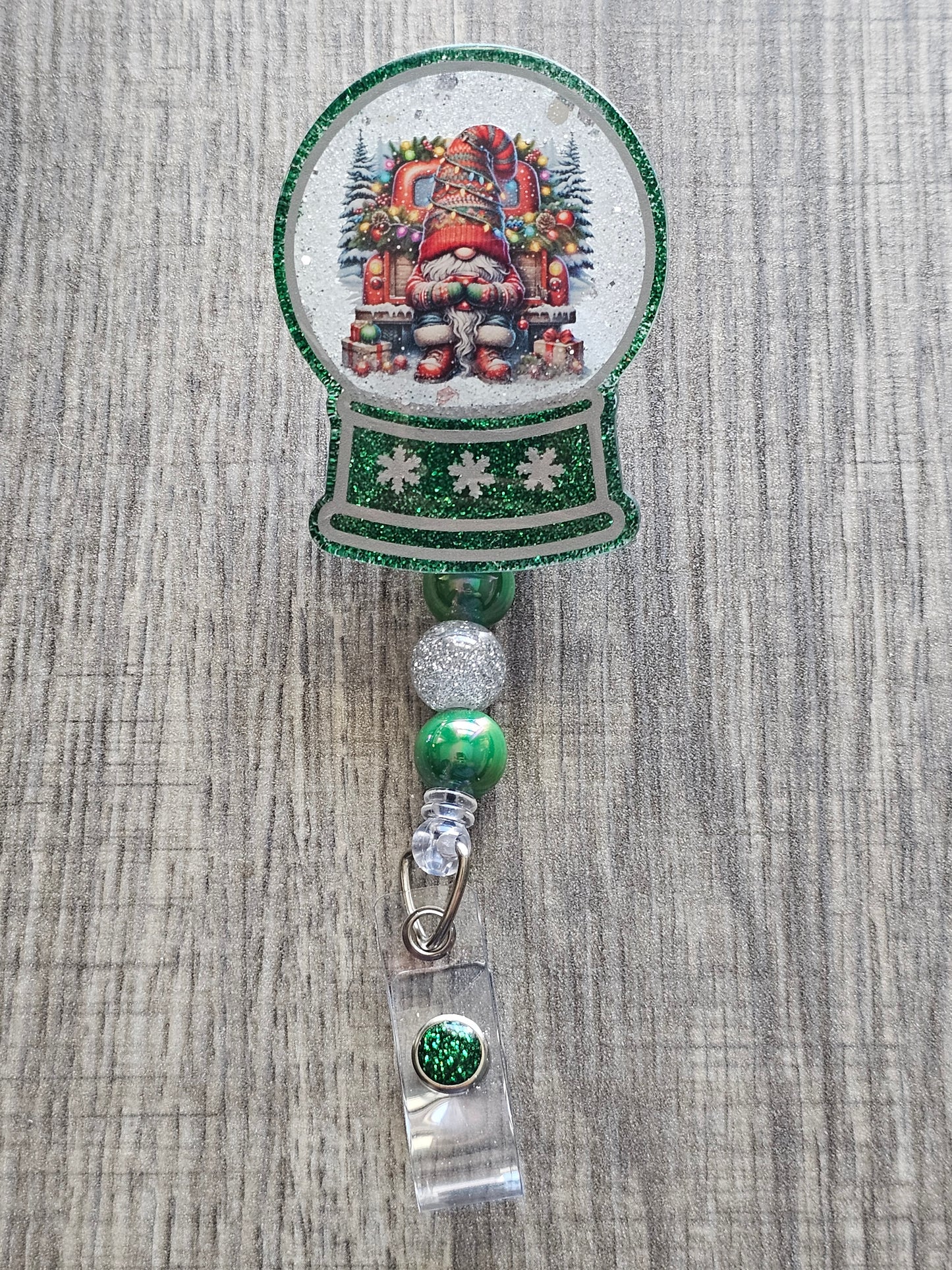 A badge reel with a snow globe design featuring a festive gnome dressed in a Christmas Sweater, drinking chocolate on the back of a truck with festive decorations surrounded by Christmas Presents. 