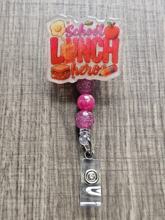 White glitter acrylic badge reel with "School Lunch Hero" text, creatively incorporating a juice box, sandwich, pencil, apple, and egg, with matching decorative beads.