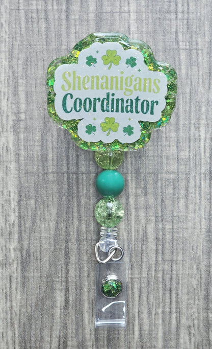 Green St. Patrick's Day badge reel with "Shenanigans Coordinator" text and festive shamrock accents.