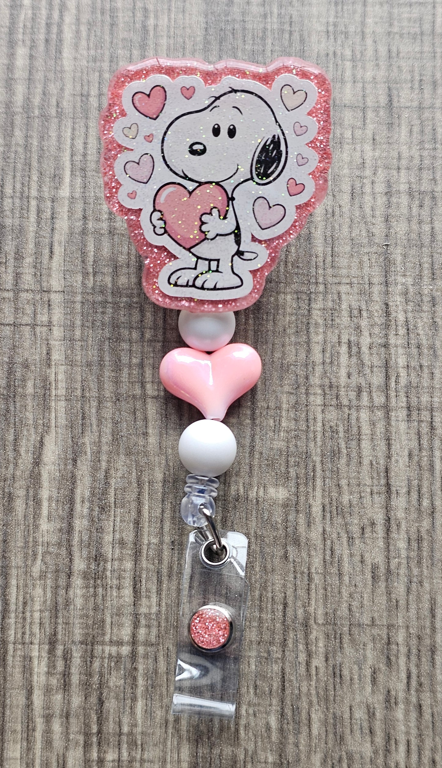 Snoopy character hugging a heart badge reel with pink decorative beads.