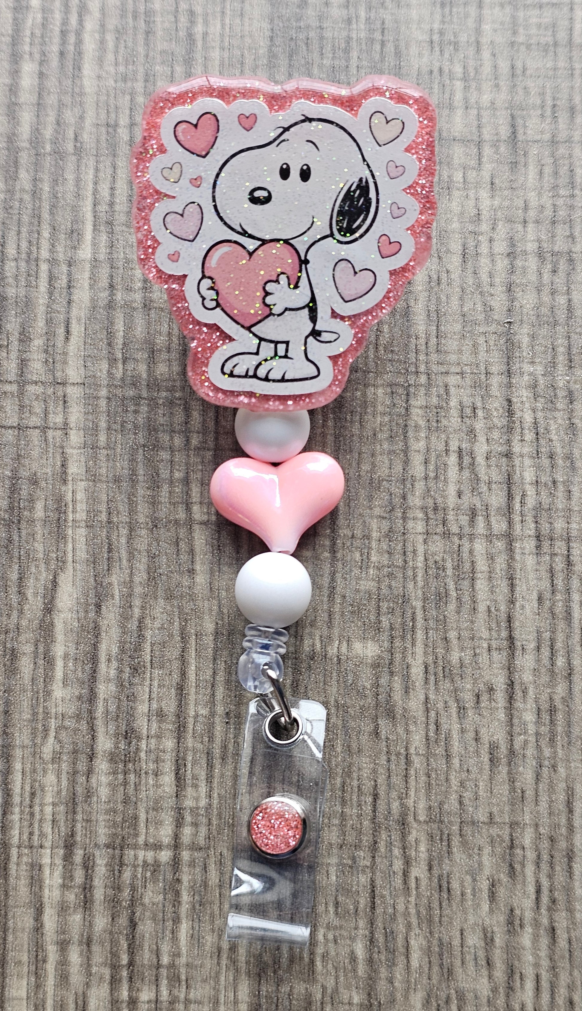 Snoopy character hugging a heart badge reel with pink decorative beads.