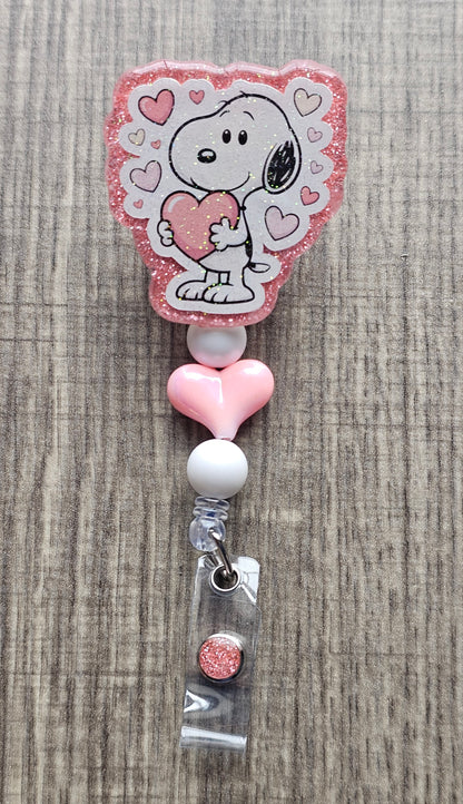 Snoopy character hugging a heart badge reel with pink decorative beads.
