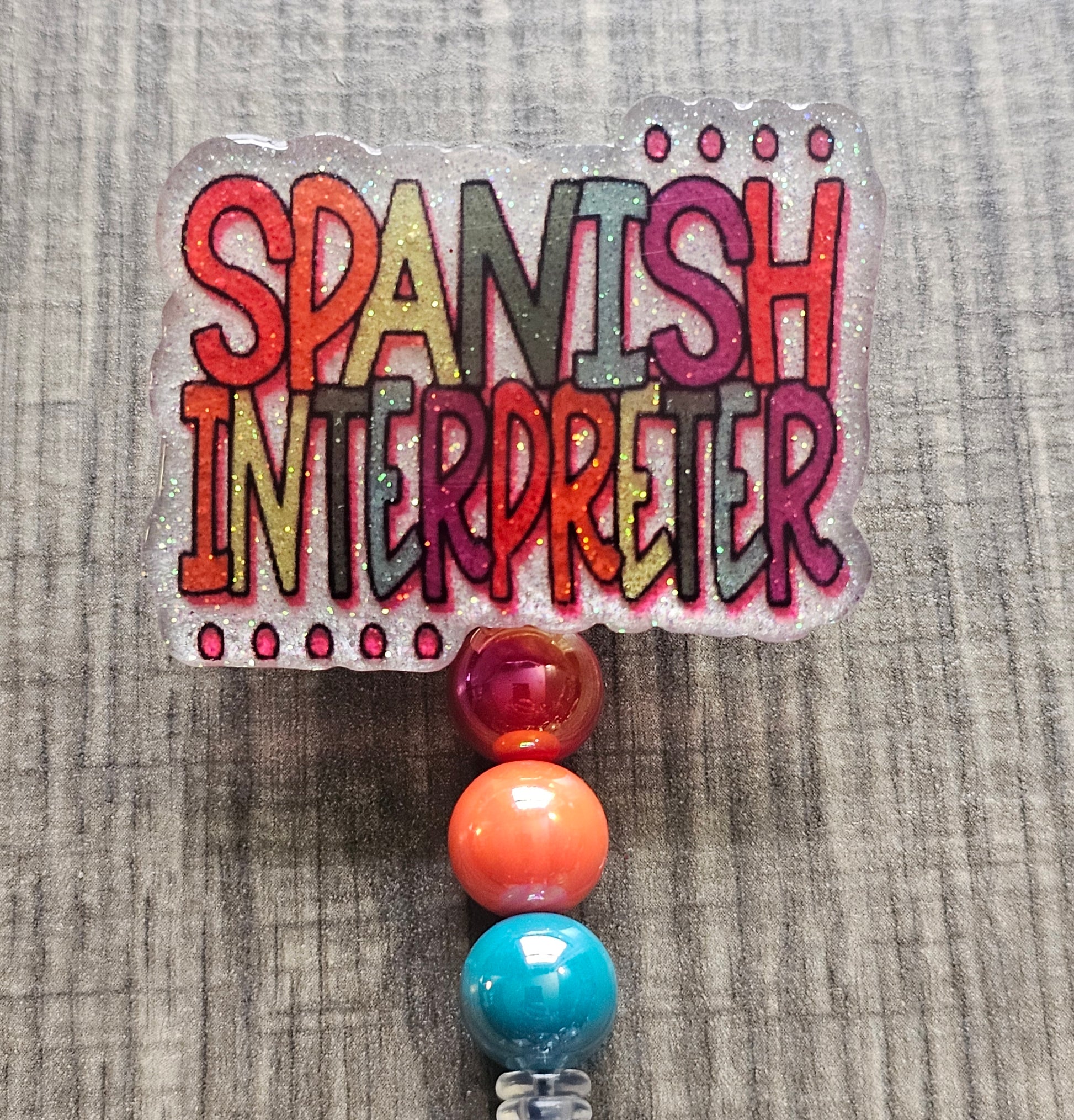 White acrylic badge reel with "Spanish Interpreter" written in colorful, creative lettering, accompanied by matching decorative beads.
