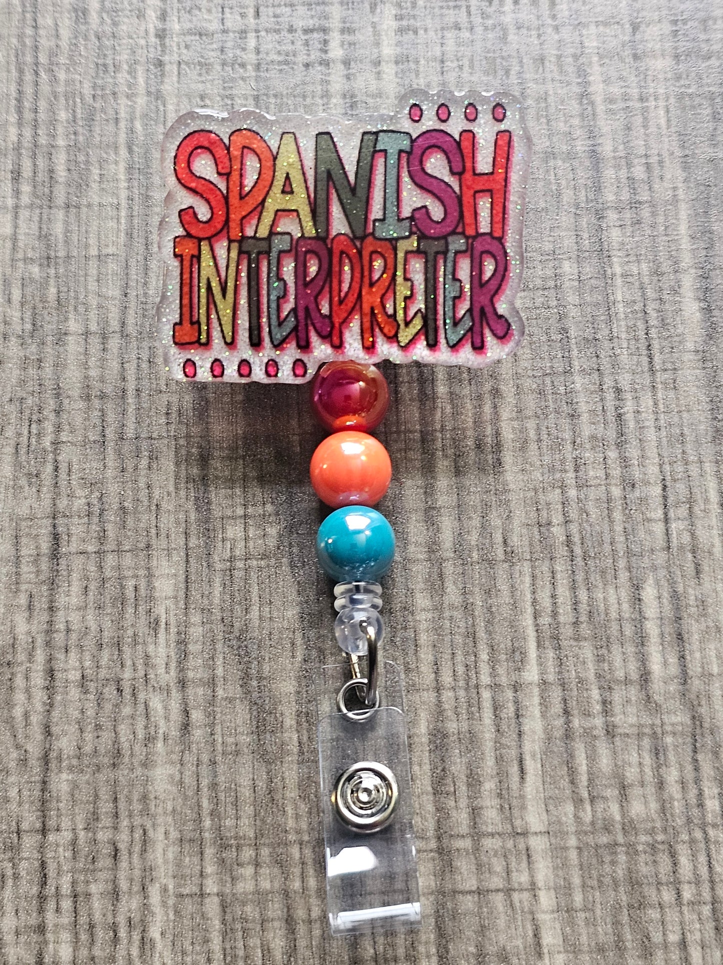 White acrylic badge reel with "Spanish Interpreter" written in colorful, creative lettering, accompanied by matching decorative beads.