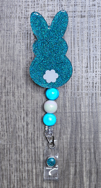 Turquoise glitter bunny-shaped badge holder with white accents on a textured gray background