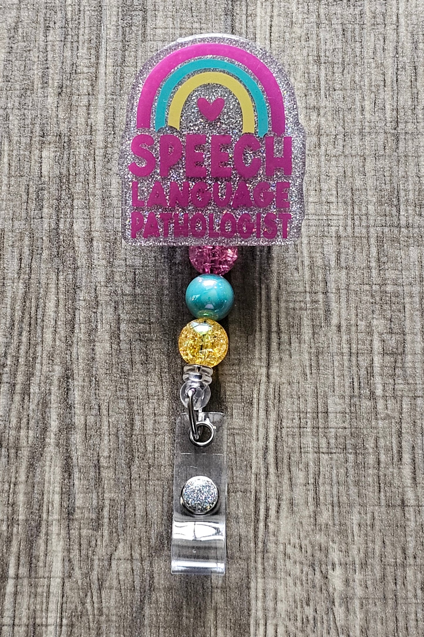 "Speech Language Pathologist" badge reel with a rainbow and a heart underneath.