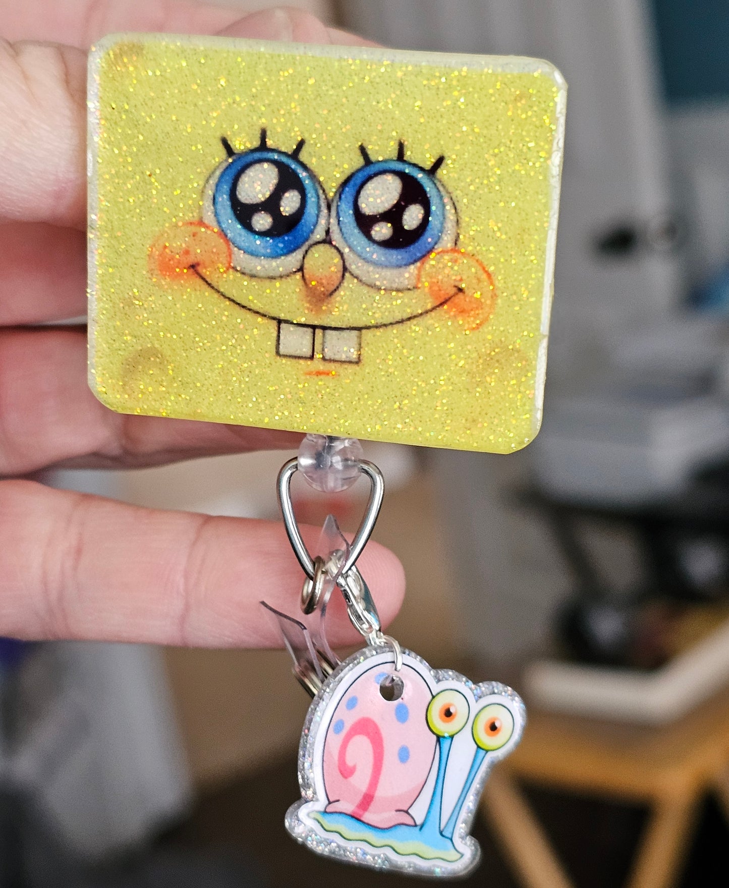 A badge reel shaped like SpongeBob’s face with a bright smile, featuring Gary the Snail as a clip attachment.