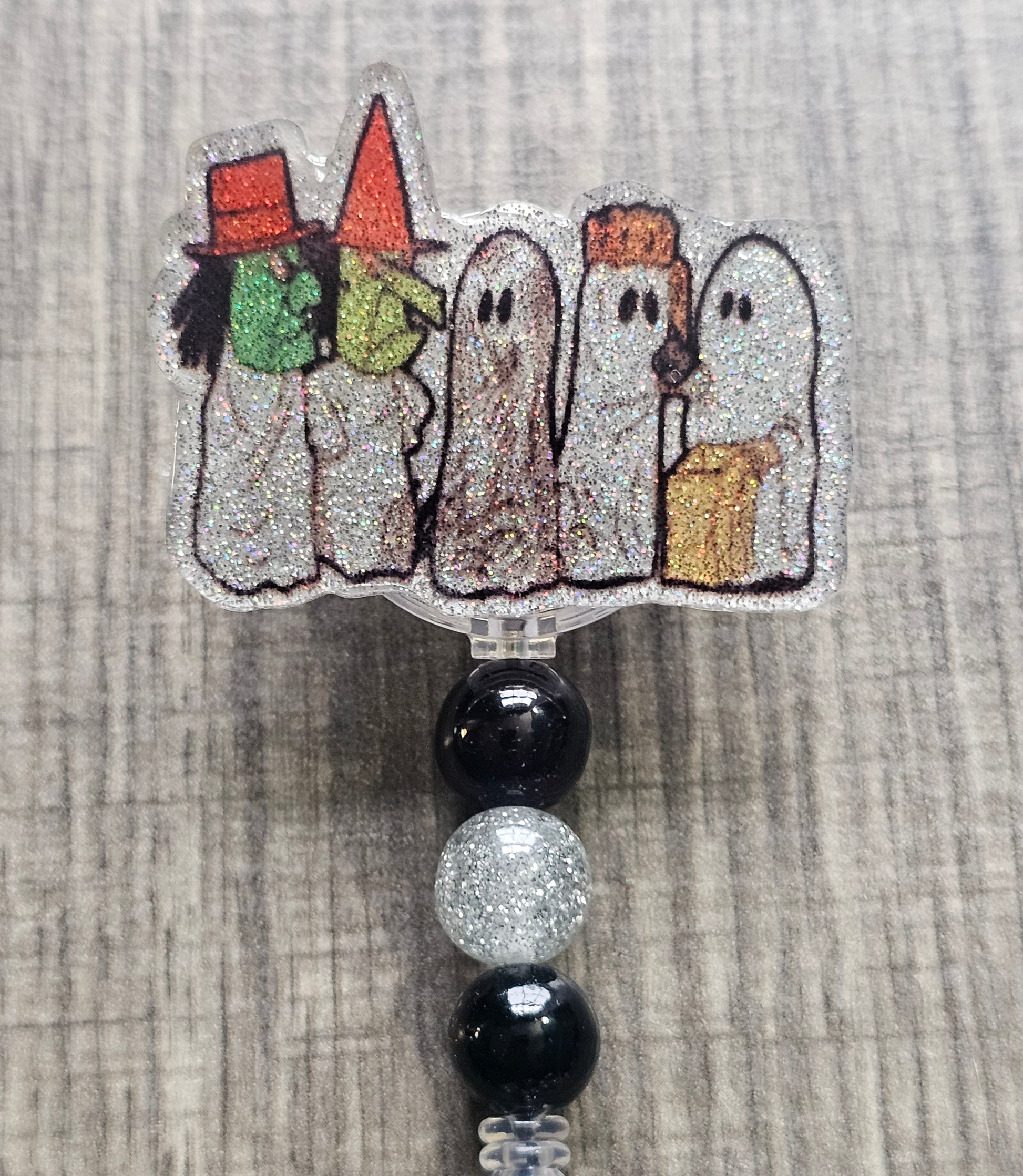 Badge reel depicting five figures in white ghost costumes, two wearing witch masks, and one holding a trick-or-treat bag, with matching decorative beads.