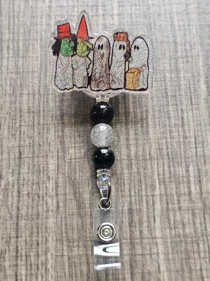 Badge reel depicting five figures in white ghost costumes, two wearing witch masks, and one holding a trick-or-treat bag, with matching decorative beads.