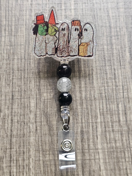 Badge reel depicting five figures in white ghost costumes, two wearing witch masks, and one holding a trick-or-treat bag, with matching decorative beads.