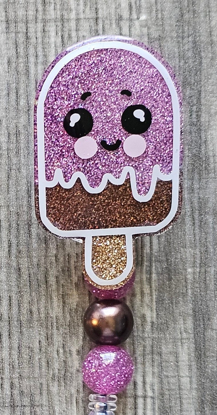 Glittery Chocolate Strawberry popsicle-shaped badge holder with a golden handle on a textured surface.