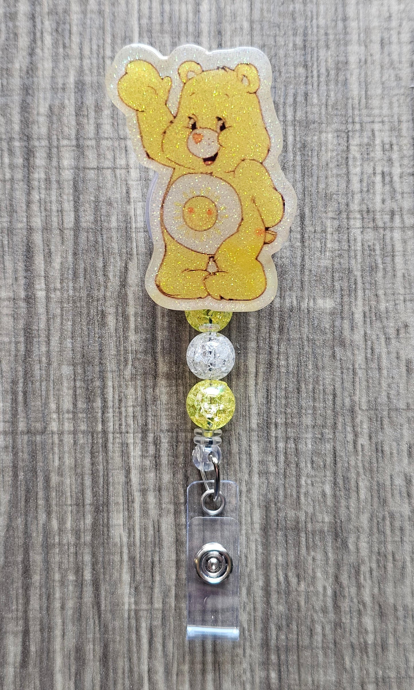 Smiling Sunshine Care Bear character badge reel with yellow and white beads on a badge holder.