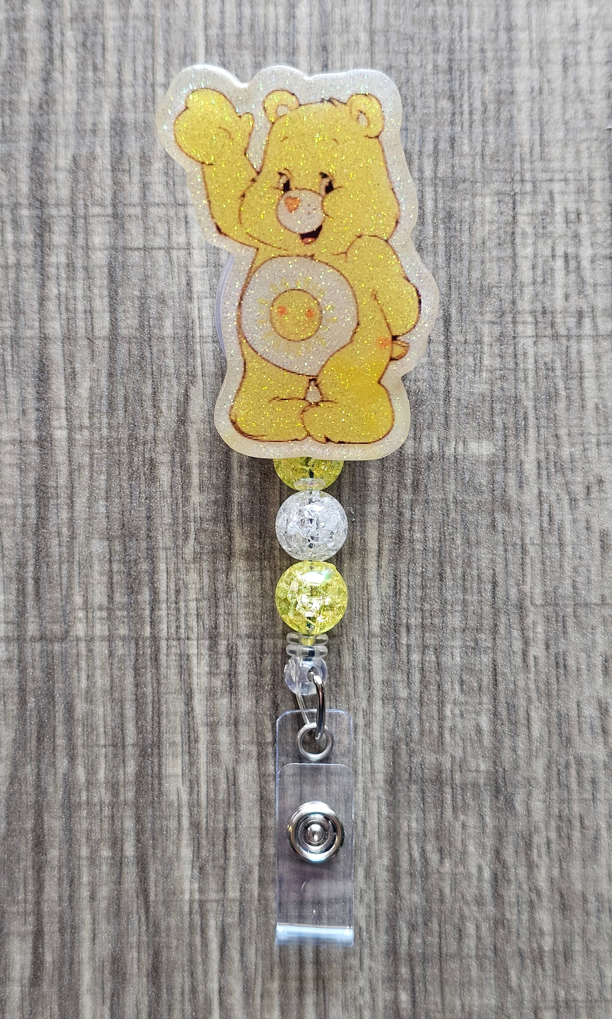 Smiling Sunshine Care Bear character badge reel with yellow and white beads on a badge holder.