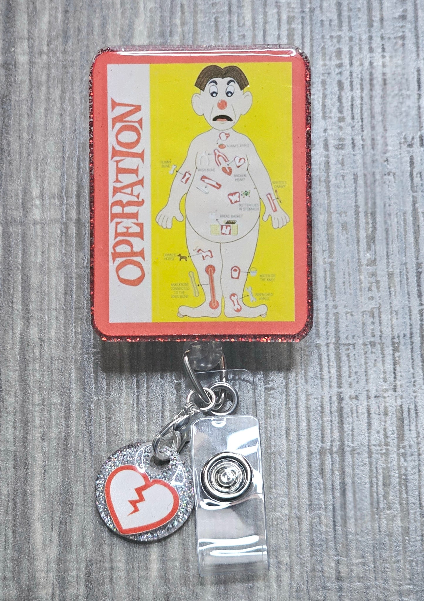 Retractable badge reel featuring the classic red-nosed patient from the Operation board game.