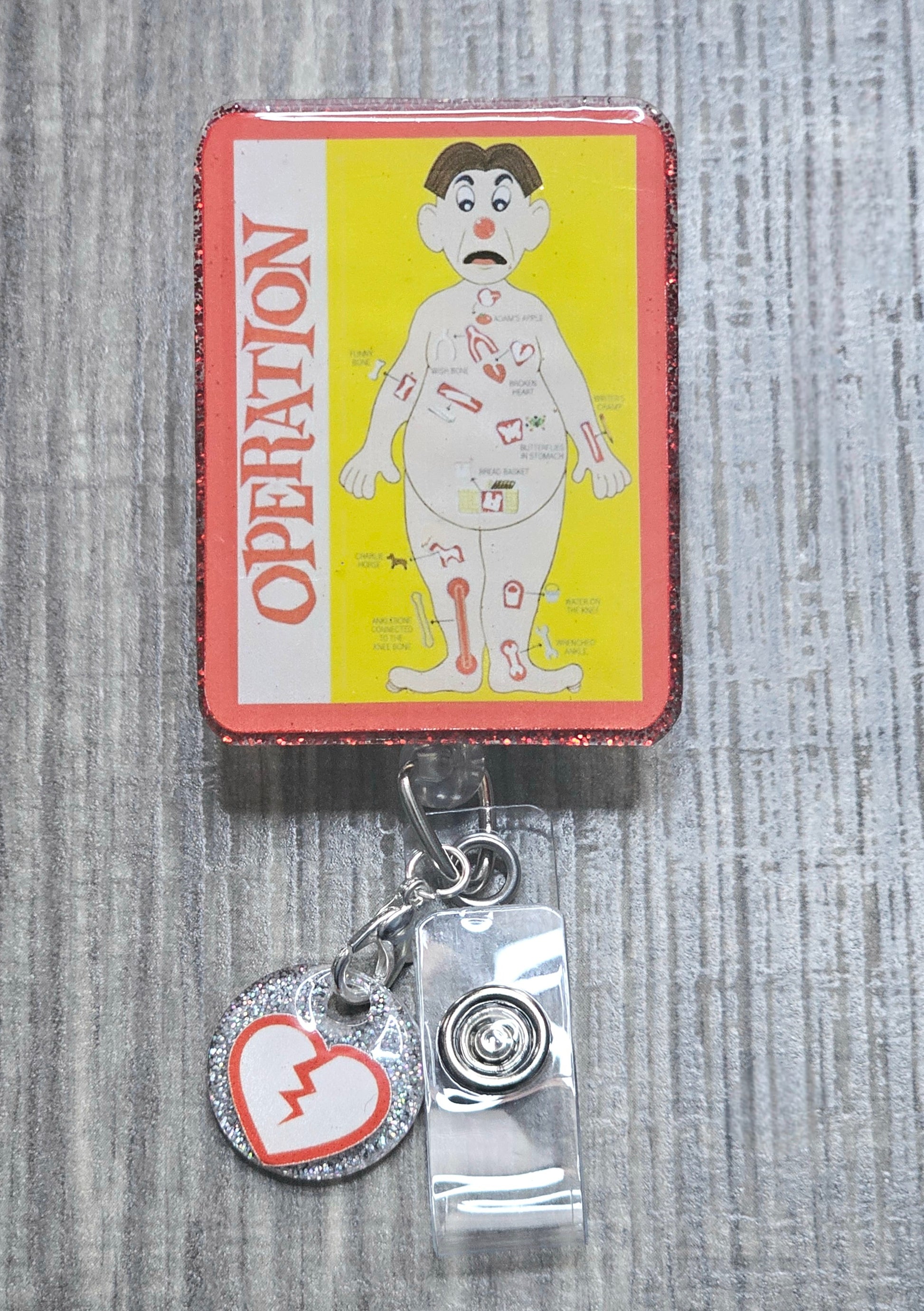Retractable badge reel featuring the classic red-nosed patient from the Operation board game.
