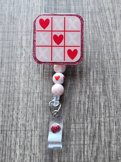 A badge reel featuring a tic-tac toe board where hearts win in honor of valentine's day 