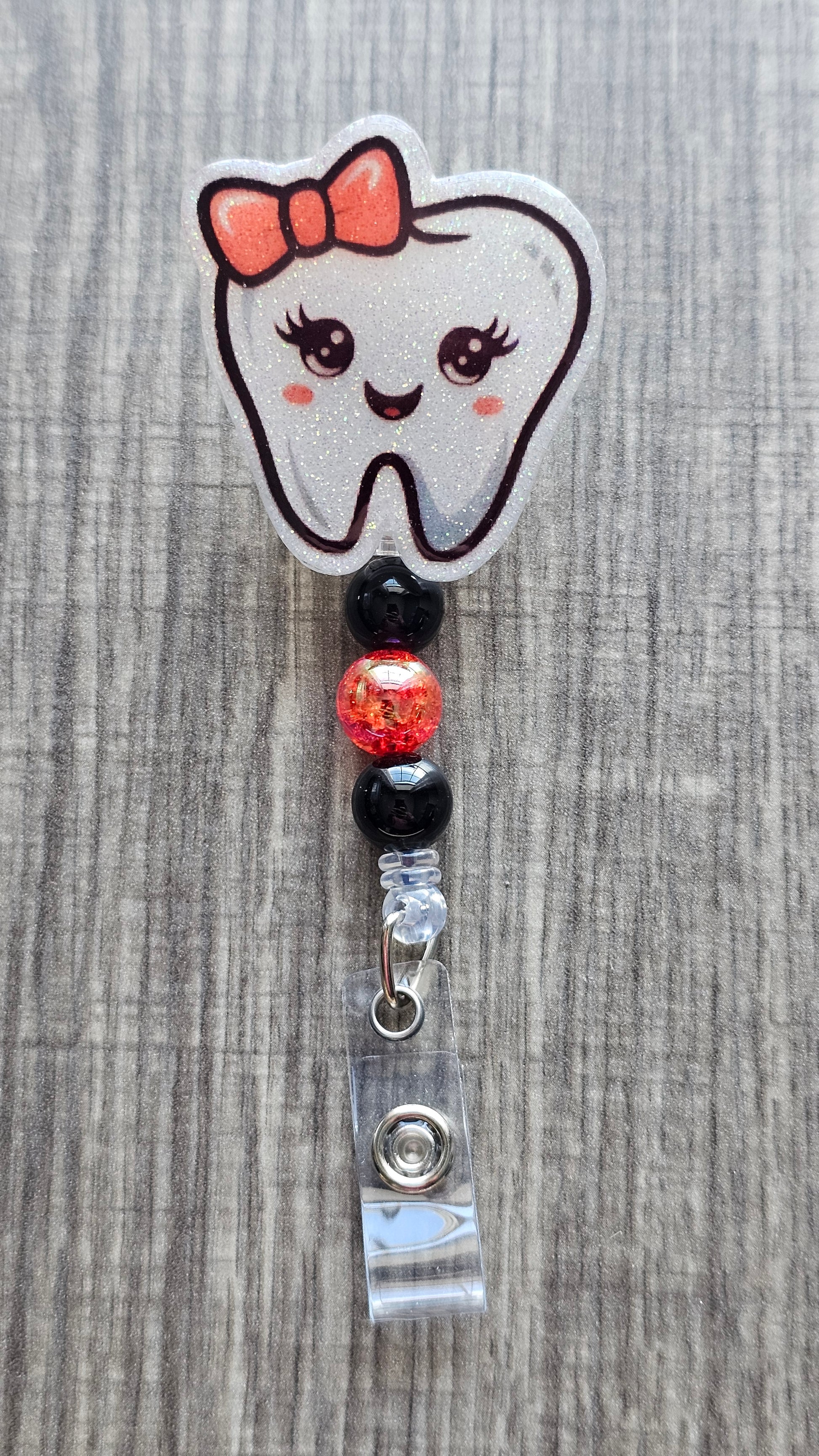Adorable tooth character with a red bow on its head and coordinating beads badge reel.