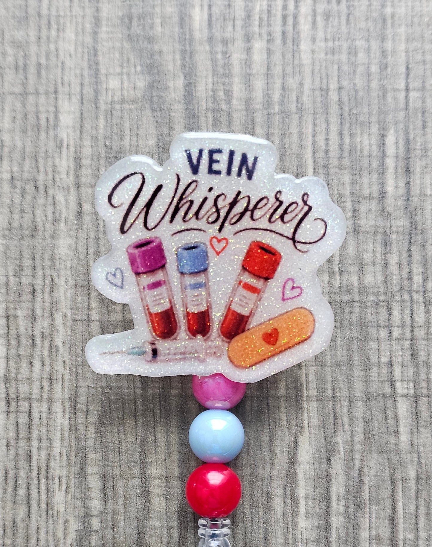 Phlebotomist badge reel featuring medical blood vials, syringe, bandage graphics, and the text Vein Whisperer with matching beads.
