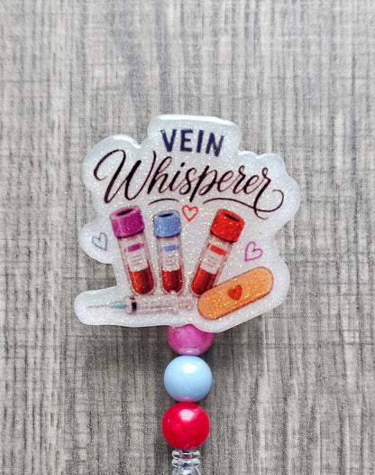 Phlebotomist badge reel featuring medical blood vials, syringe, bandage graphics, and the text Vein Whisperer with matching beads.