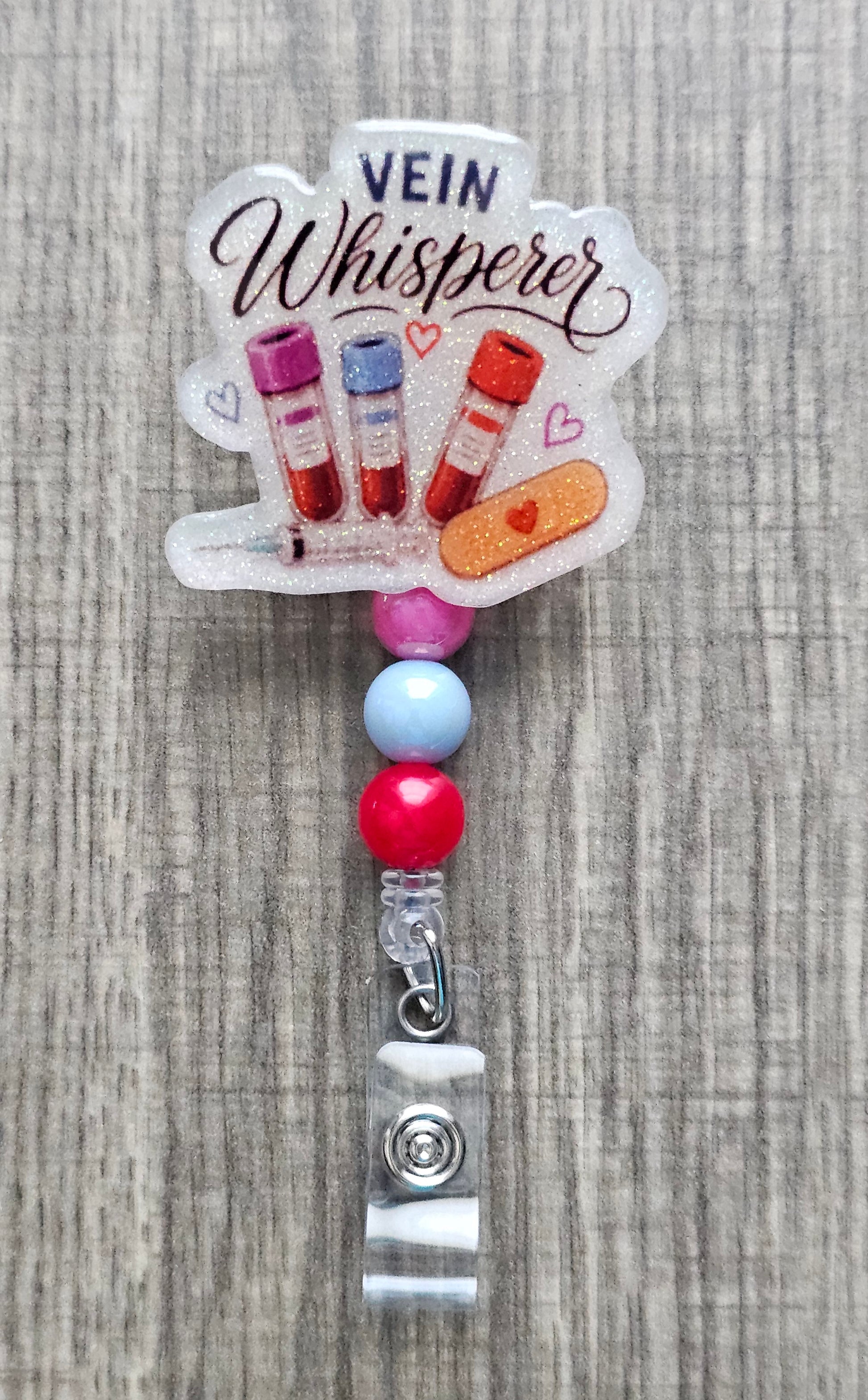 Phlebotomist badge reel featuring medical blood vials, syringe, bandage graphics, and the text Vein Whisperer with matching beads.