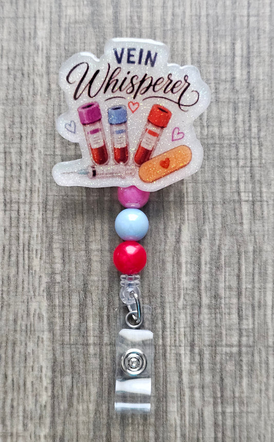Phlebotomist badge reel featuring medical blood vials, syringe, bandage graphics, and the text Vein Whisperer with matching beads.
