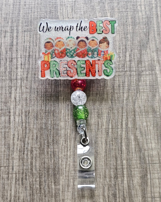 A badge reel stating we wrap the best presents with the design incorporating some adorable children wrapped in cozy festive blankets