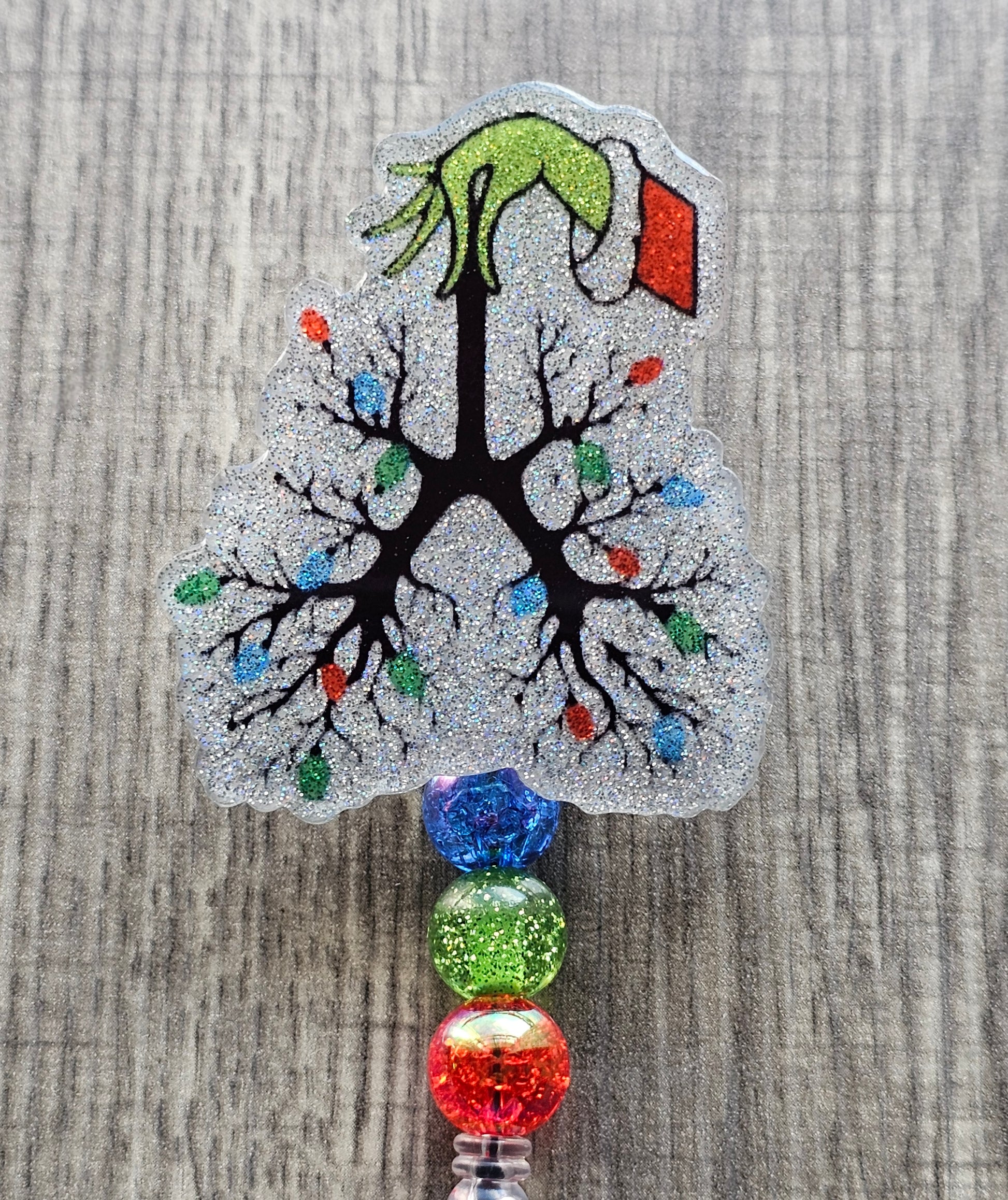 A Badge reel shaped like a pair of lungs, this design features a whimsical grinch hand holding the respiratory system, styled as branches adorned with vibrant Christmas lights.