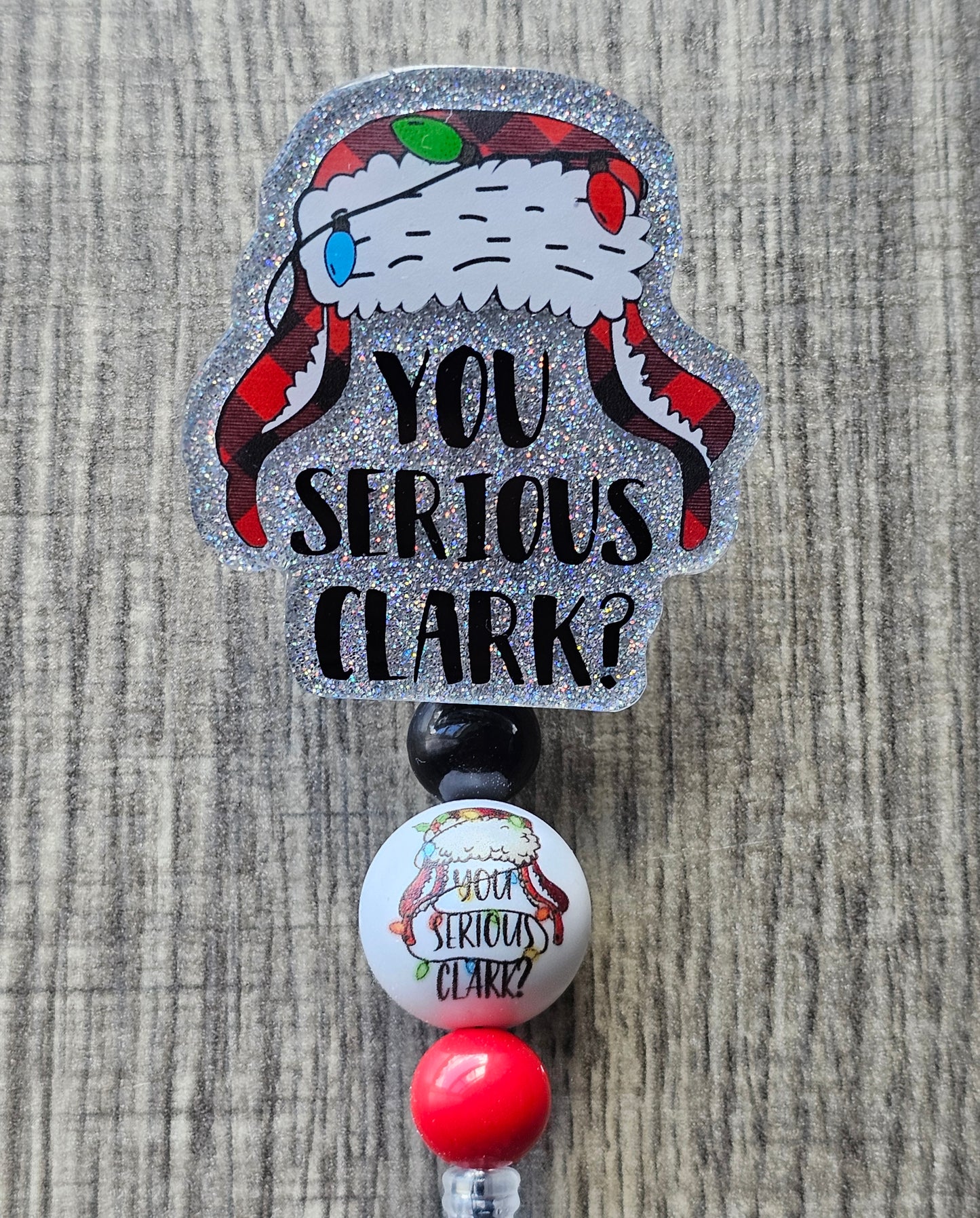 A Badge Reel featuring a Christmas themed winter hat wrapped with Christmas lights and underneath it with the words You Serious Clark? 