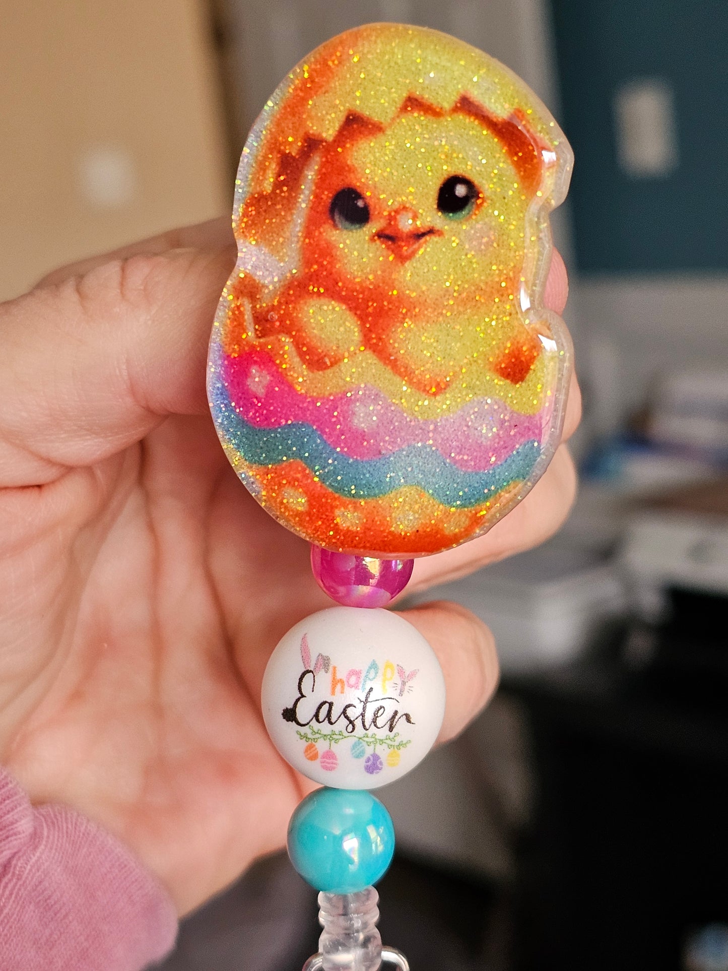 A badge reel featuring a baby duck hatching from a colorful Easter egg, available in two variants.