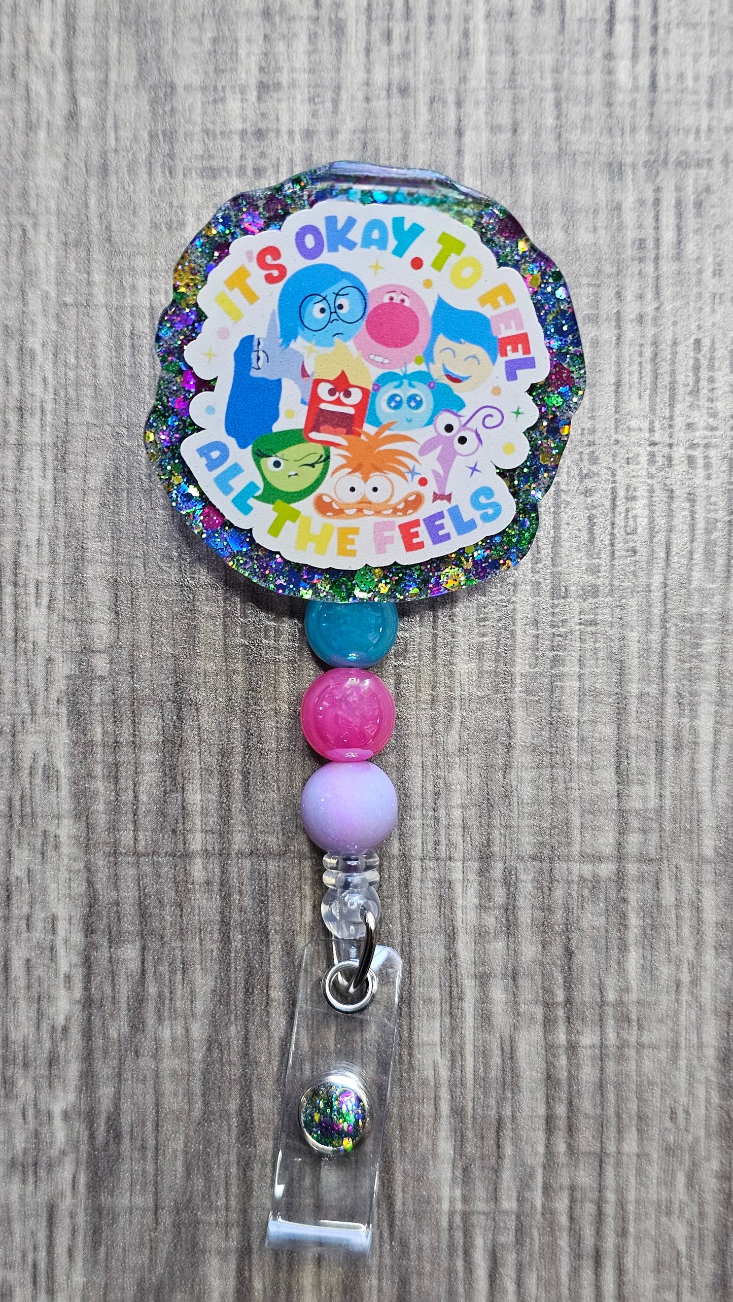  Inside Out movie characters clustered together with text "It's okay to feel all the feels" on a retractable badge reel.
